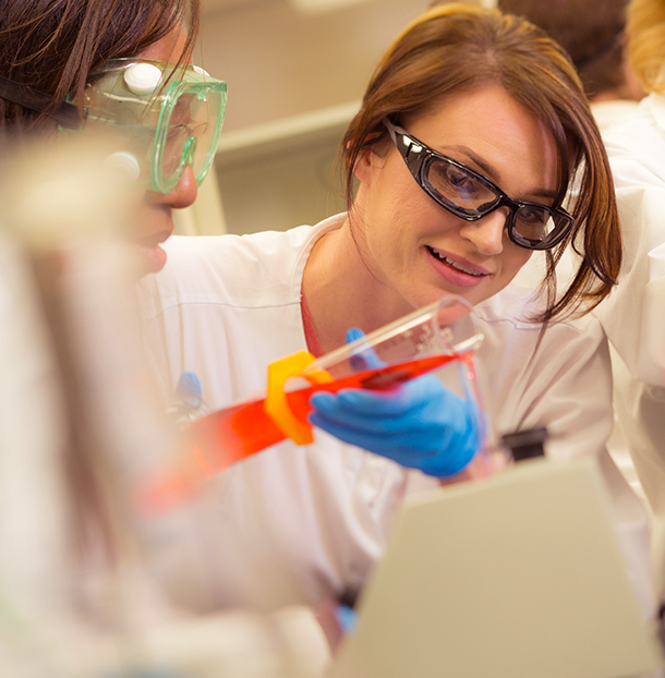 A woman in lab coat and goggles holding a pair of scissors.