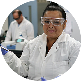 A woman in lab coat and goggles holding a tube.