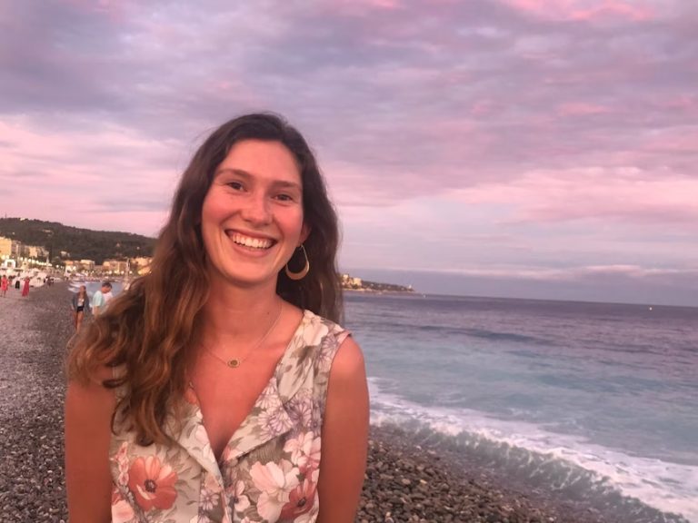A woman standing on the beach smiling for a picture.