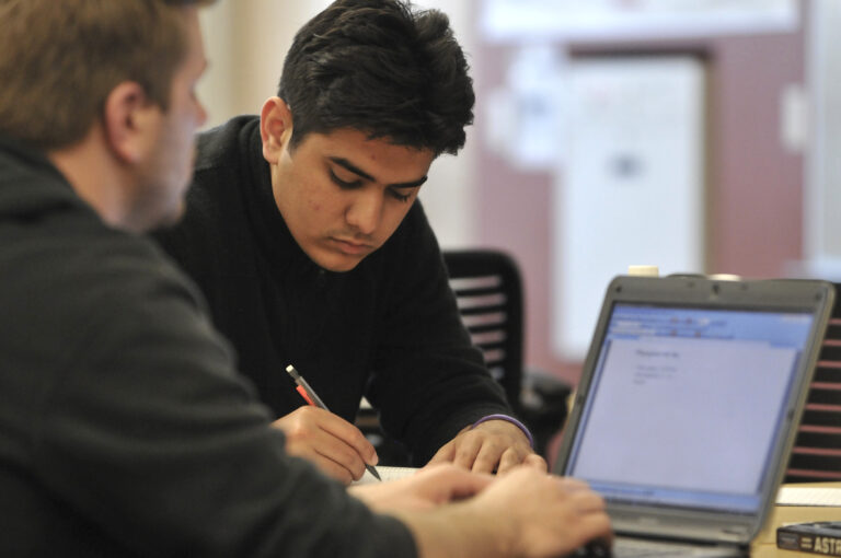 Two men are working on a laptop together.